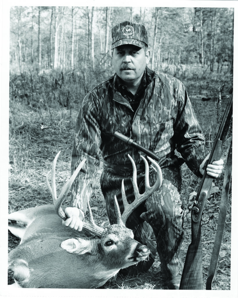 Una foto en blanco y negro de un hombre, un ciervo y un rifle de avancarga