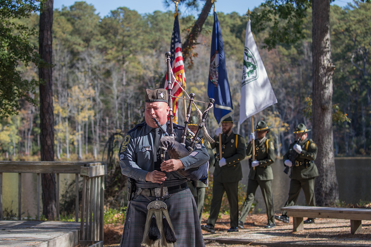 Una imagen de un hombre con gaita liderando una ceremonia de dedicación de la guardia de honor del DWR en un bosque caducifolio