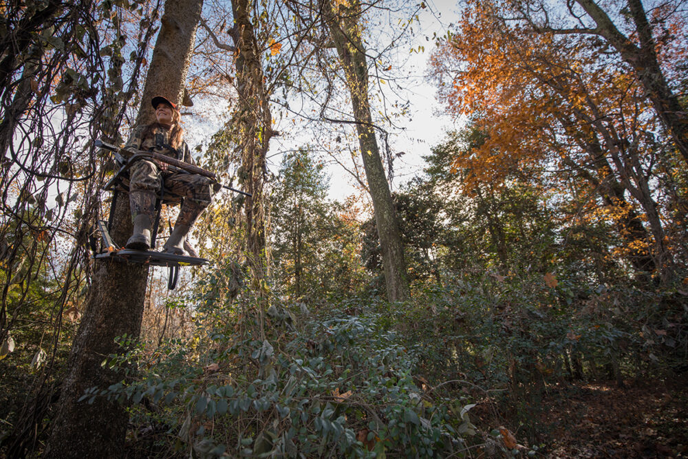 Una imagen de la misma mujer sentada en un árbol con una pistola vigilando a los ciervos
