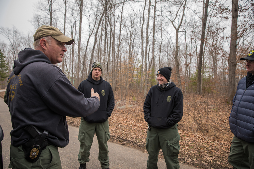 Un grupo de 4 personas paradas en la carretera hablando sobre el entrenamiento de perros de rastreo