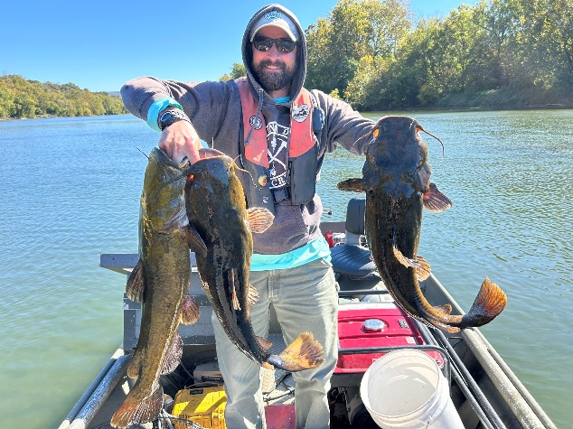 Un pescador en una barca sosteniendo un bagre de cabeza plana en el cauce principal del río Shenandoah.
