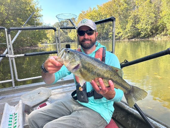Un pescador en una barca sosteniendo una lubina de boca grande en el río South Fork Shenandoah.