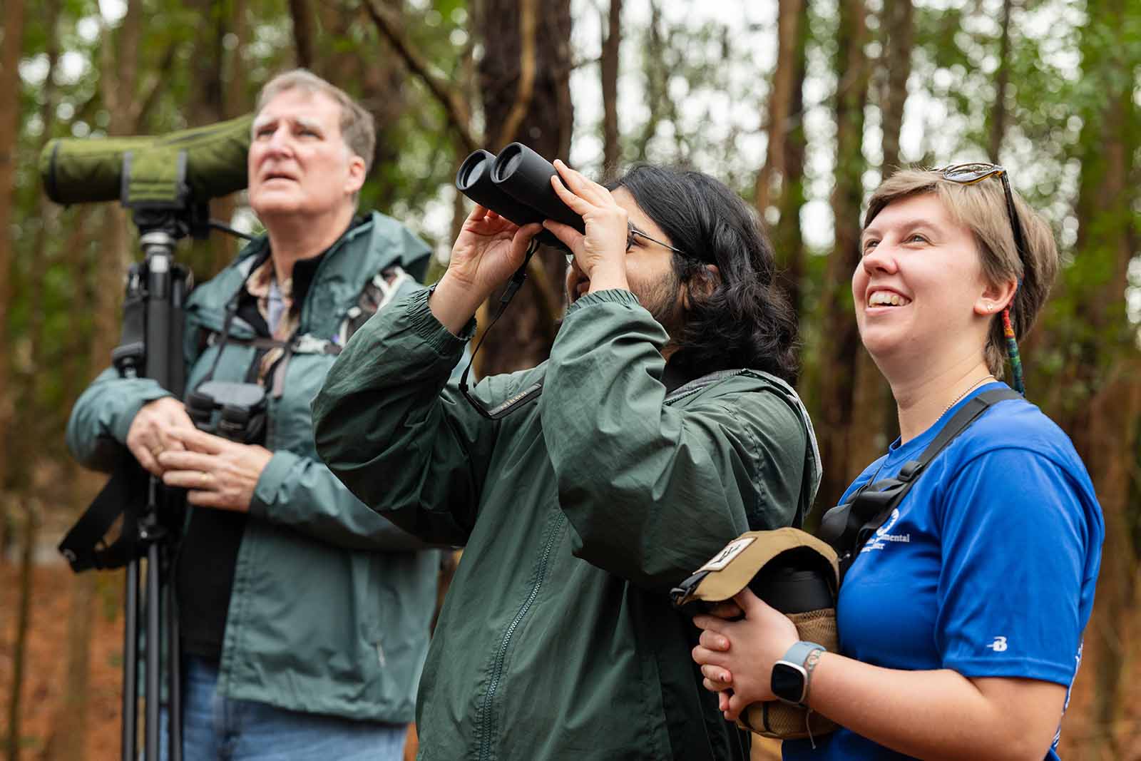 Dos personas con chaquetas verde oscuro mirando hacia arriba, una de ellas con un par de prismáticos