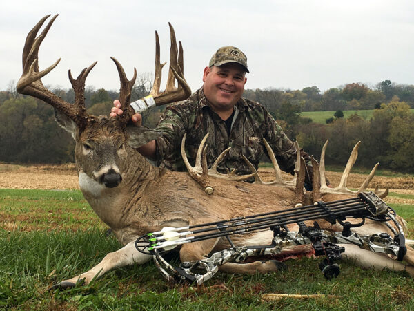 Una imagen de un cazador junto a un ciervo toro que había matado con arco y flecha