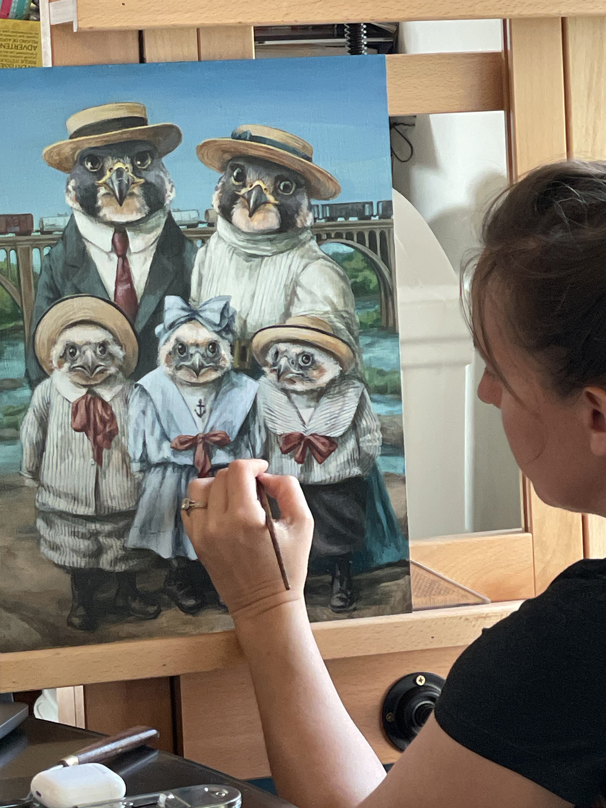 Una foto de una mujer pintando un cuadro grande de dos halcones peregrinos adultos y tres juveniles vestidos con ropa frente al río James en Richmond.