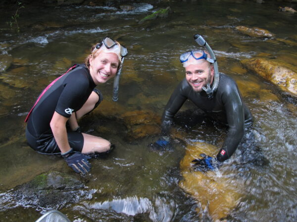Dos personas parcialmente sumergidas en el agua y con trajes de neopreno y tubos.