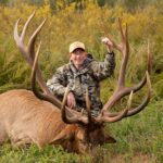 Hombre sonriendo con su presa, un alce.