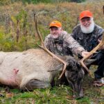 Dos hombres posando con un alce muerto.