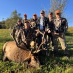 Un grupo de siete hombres posando con un alce muerto en un campo.