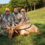Tres hombres posando, arrodillados, con un alce muerto.