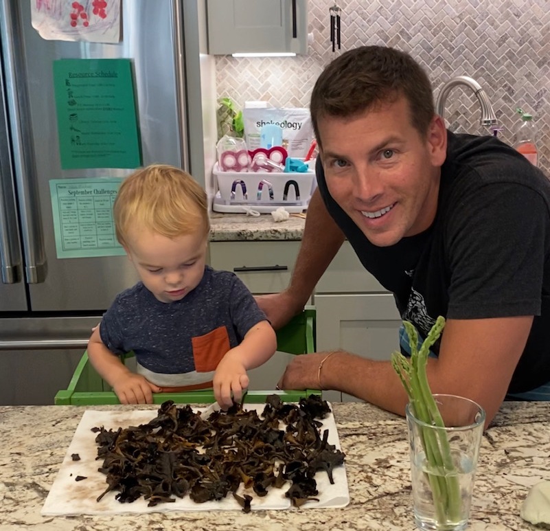Una imagen de un niño junto a un montón de setas y su padre