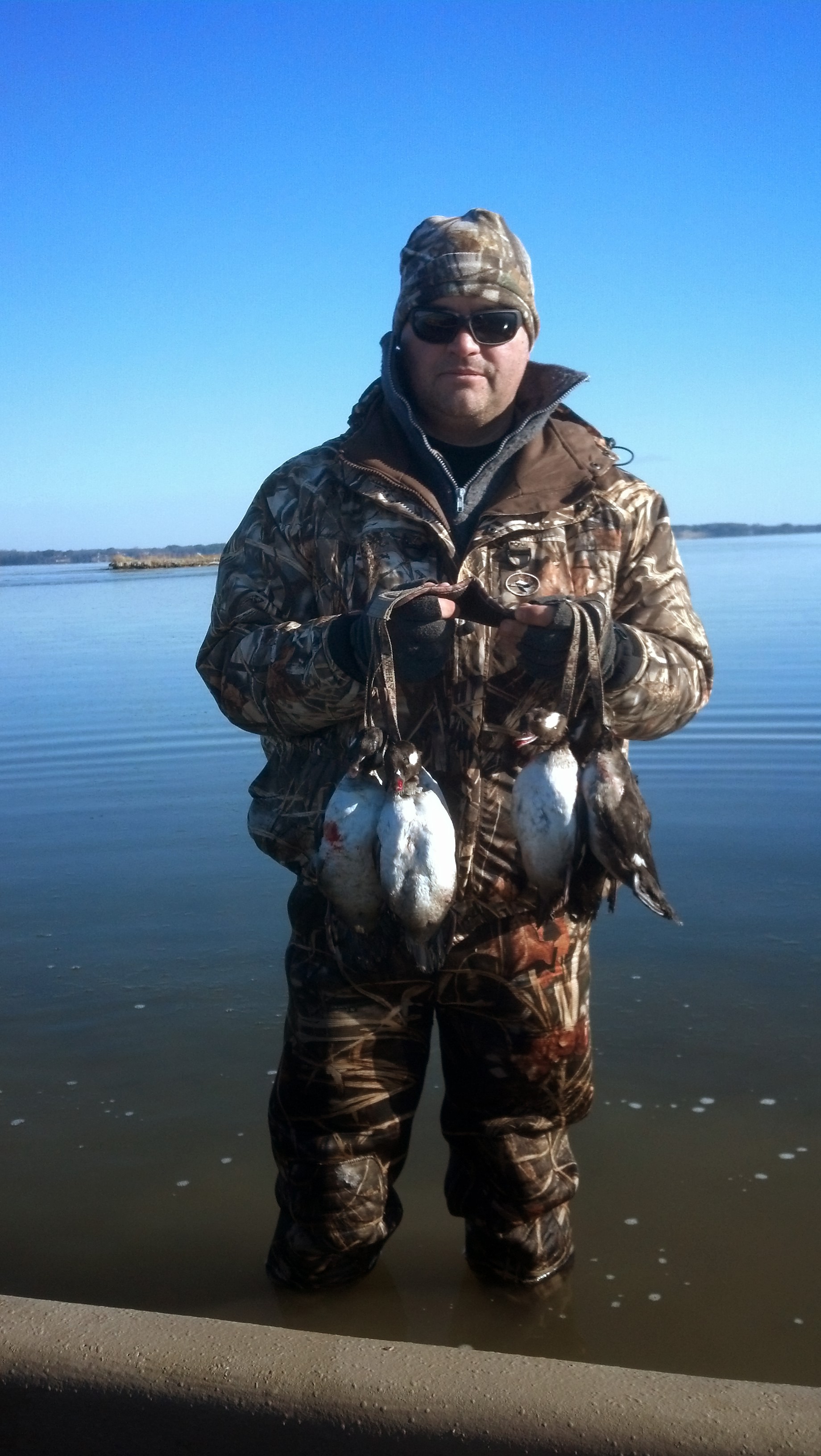 Una imagen de un hombre en agua helada sosteniendo un montón de patos muertos