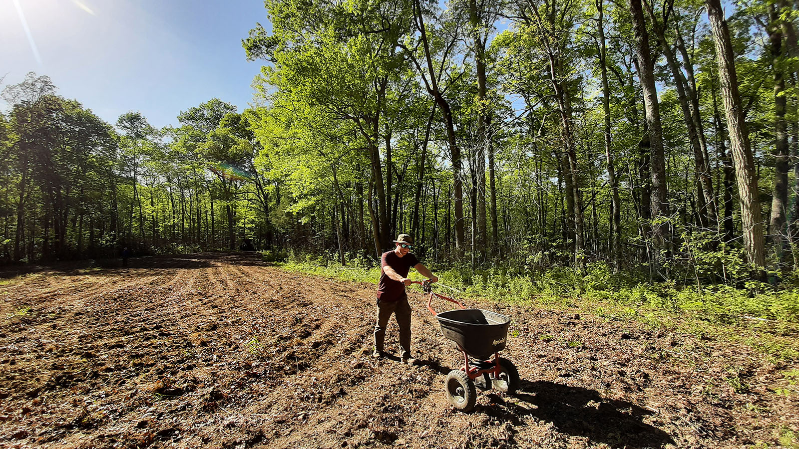 Imagen de un hombre preparando un campo para la restauración de la pradera; Actualmente está esparciendo semillas en el suelo removido