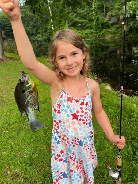 Una niña, de 6años, sostiene un pez en un sedal sonriendo para la cámara.