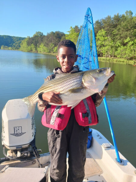 Un niño de 6años, sosteniendo un gran pez en sus brazos en un bote.