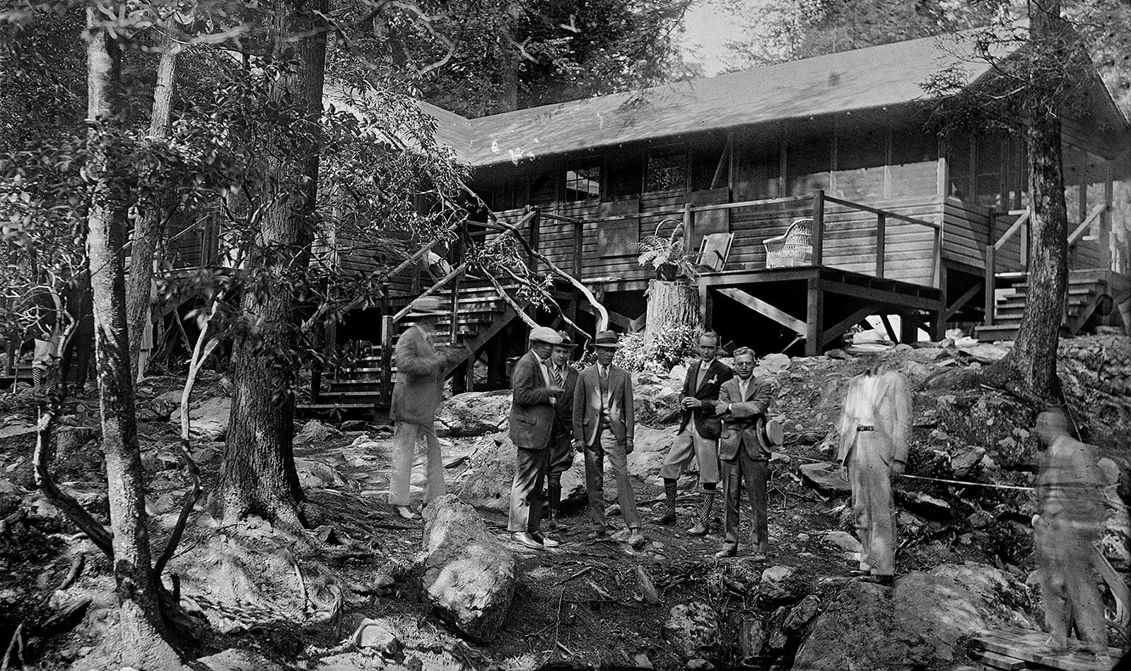 Una foto en blanco y negro de un grupo de personas con ropa de 1930época de la década de 1970 de pie frente a The Brown House, una residencia de madera construida sobre un mirador del río Rapidan.