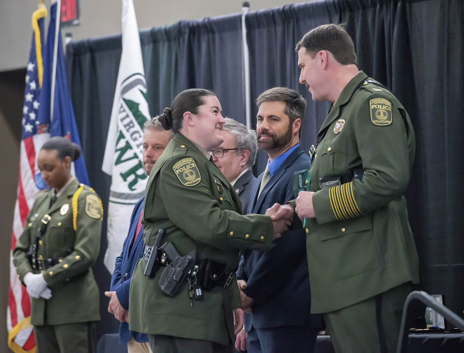 Una foto de una oficial de policía de conservación en uniforme aceptando un premio de un CPO masculino en uniforme y un hombre en traje.