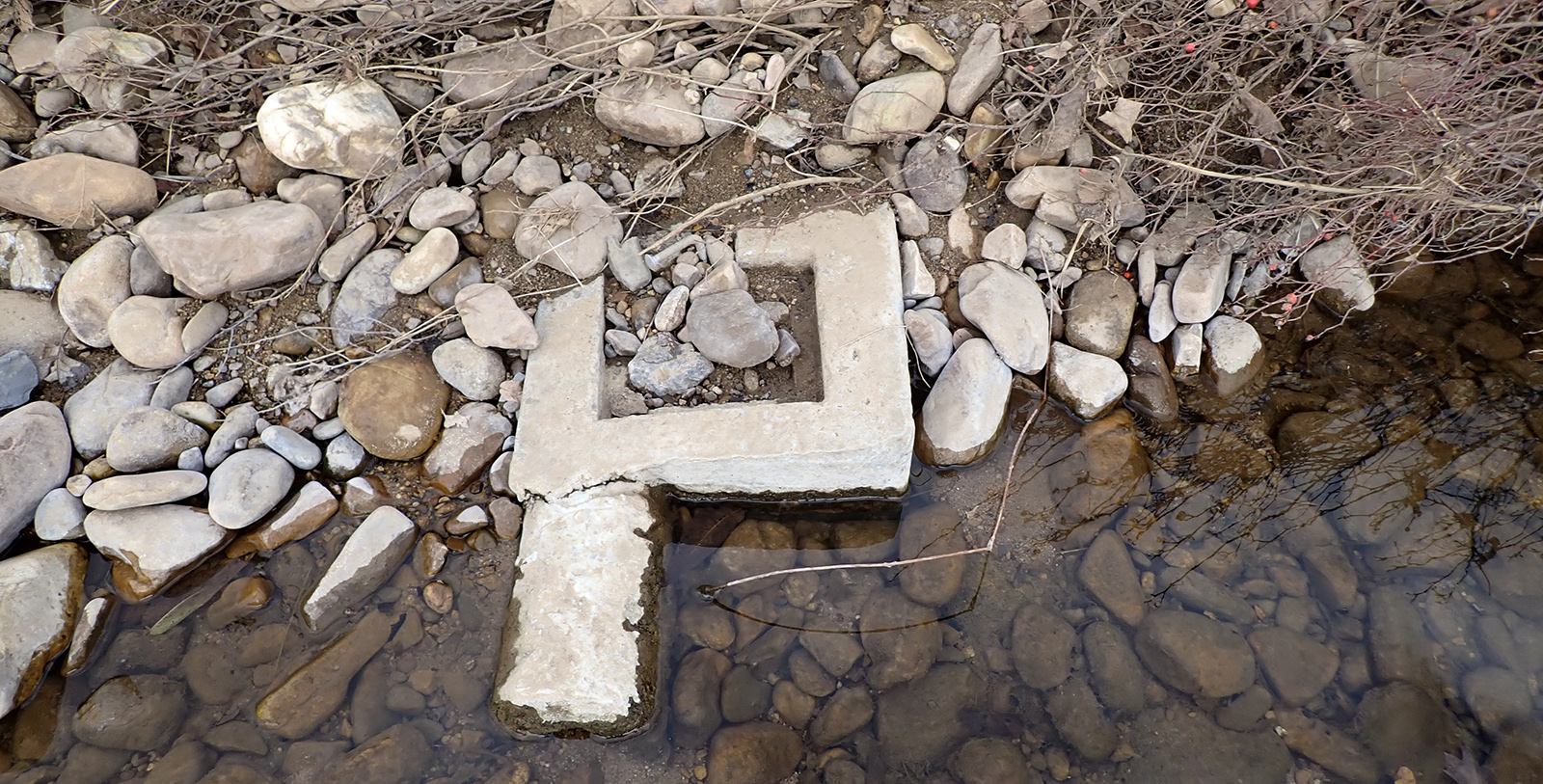 Una foto de un cuadrado de hormigón al borde de un arroyo con rocas encima.