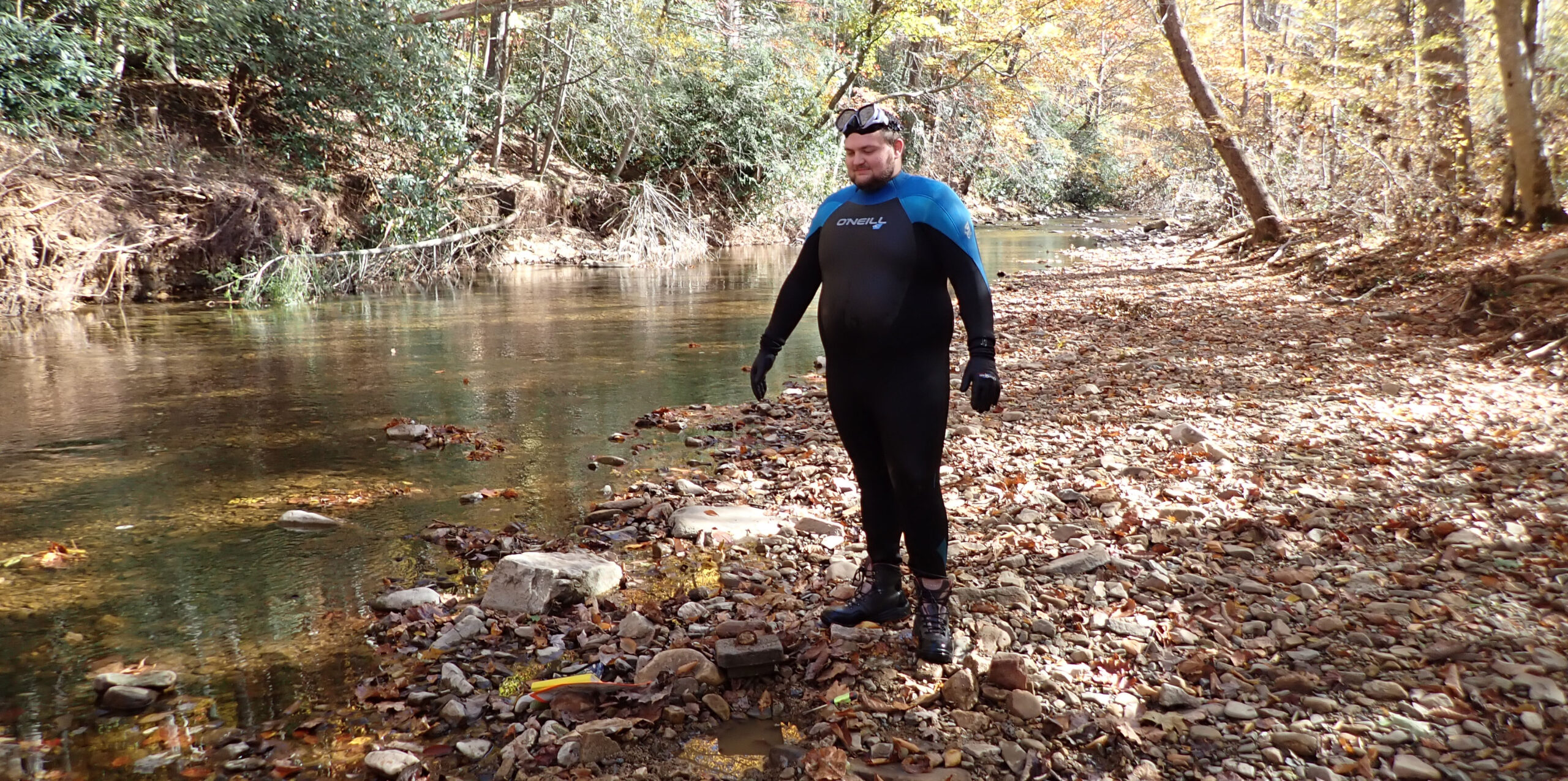 Una foto de un arroyo con una gran extensión de roca expuesta a un lado, con un hombre de pie sobre las rocas con un pequeño cuadrado de concreto a sus pies.