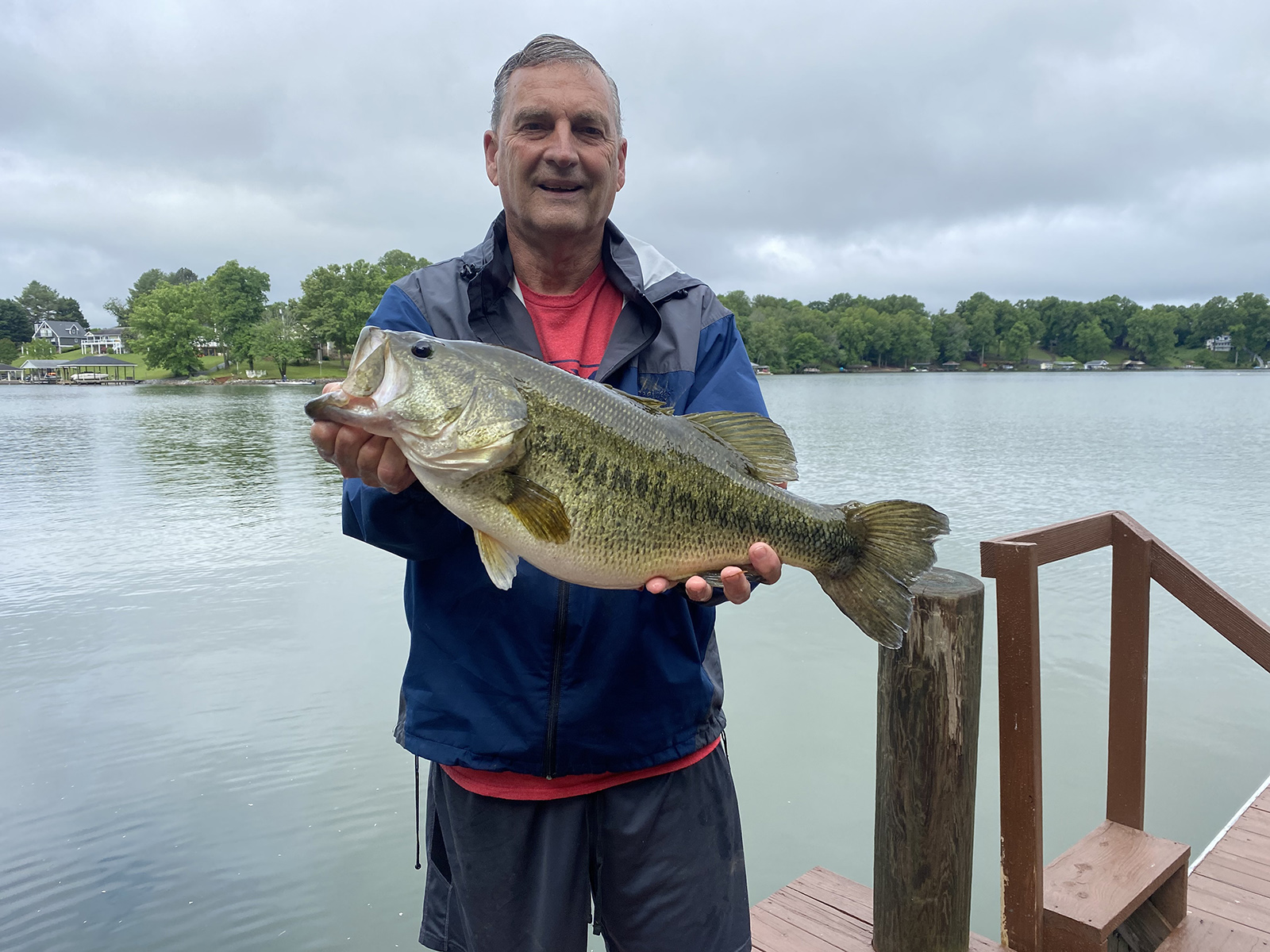 Una foto de un hombre parado en un muelle frente a un lago sosteniendo una lubina bocazas muy grande.