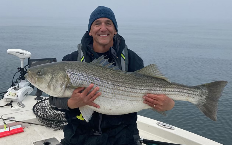 Una foto de un hombre sonriente sosteniendo un enorme pez mientras está de pie en un barco.
