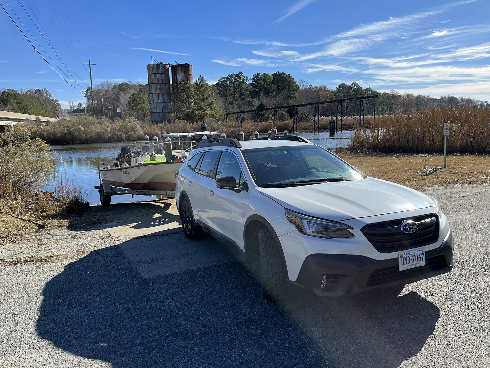 Un coche blanco tirando de un pequeño bote, retrocediendo por una rampa para botes hacia un río.