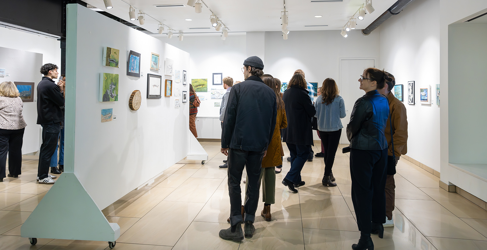 Una foto de un grupo de personas viendo obras de arte colgadas en las paredes.