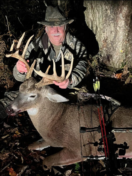 Una foto de un hombre camuflado con un lazo que sostiene las astas de un gran ciervo cazado.