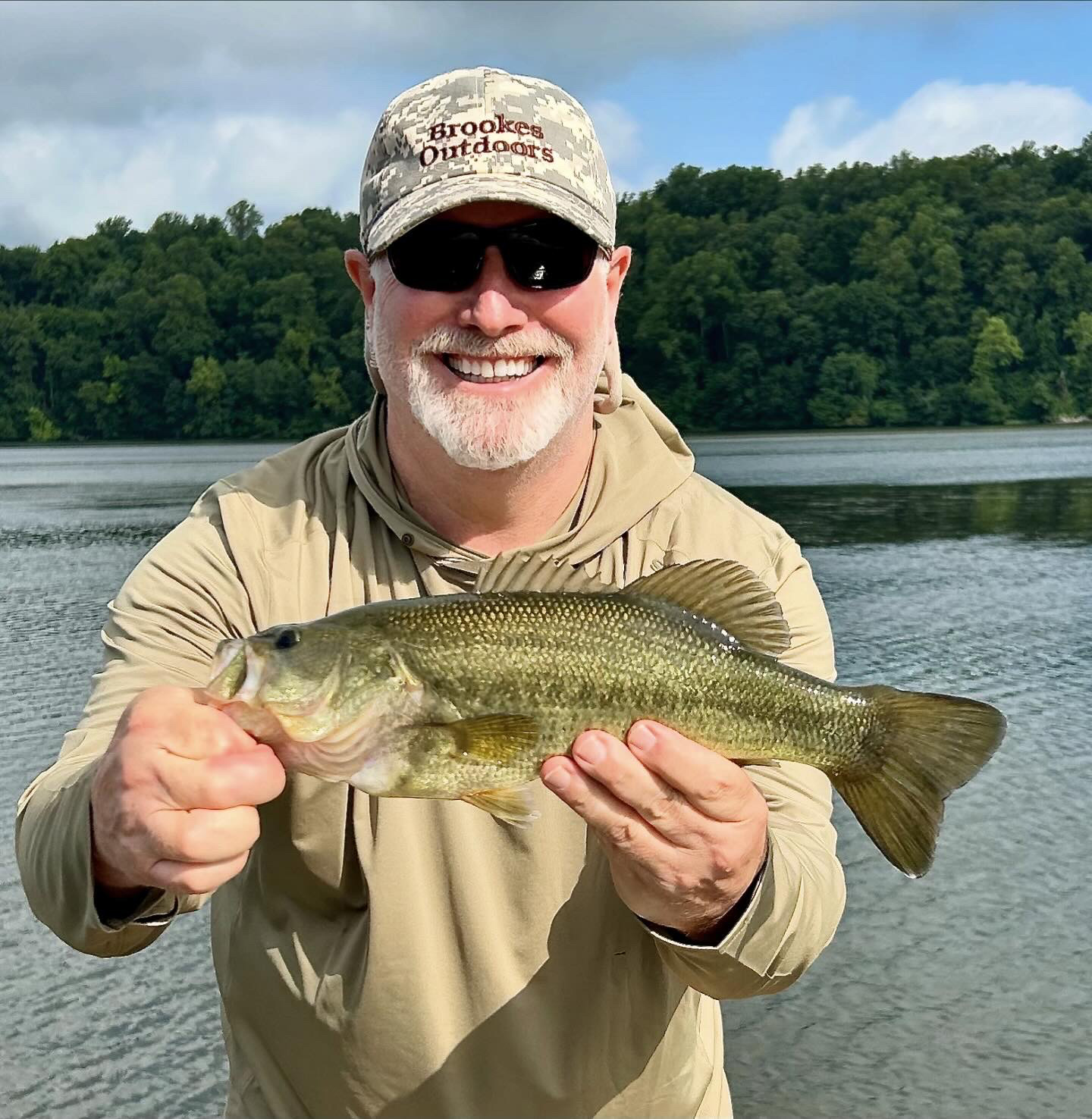 Una foto de un hombre sonriente sosteniendo una lubina con un río al fondo.