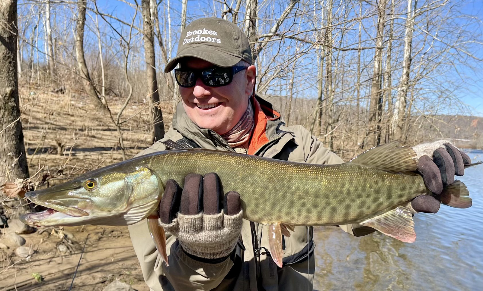 Una foto de un hombre sosteniendo un gran pez almizclado fuera del agua y sonriendo.