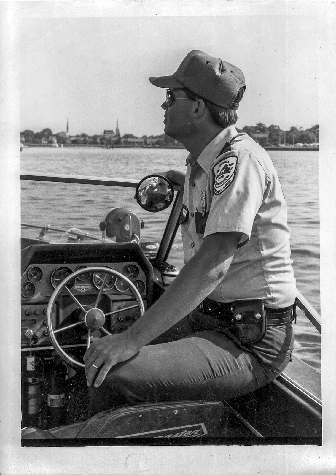 Una foto en blanco y negro de un hombre con uniforme de guardabosques pilotando una pequeña embarcación.