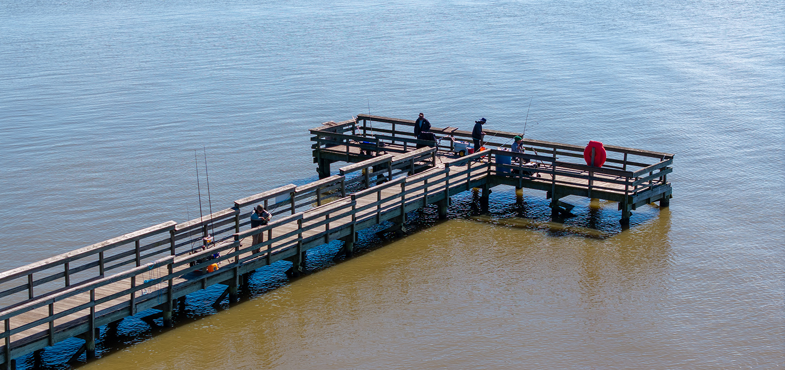 Una foto aérea de un gran muelle de pesca en forma de T en el agua de un río.