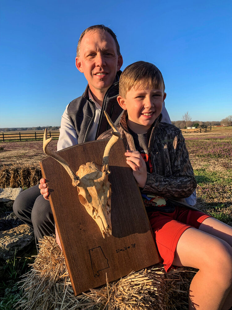 Una imagen de un hombre y su sol sosteniendo un cráneo de ciervo enmarcado que fue el primer ciervo al que dispararon juntos