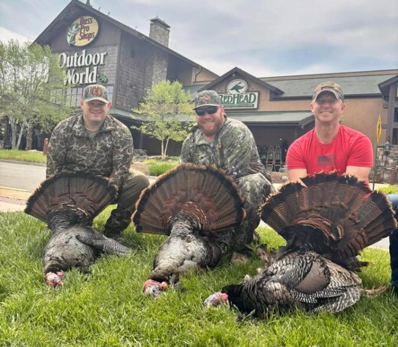 Una foto de tres hombres y tres pavos muertos en el césped frente a una tienda Bass Pro Shop.