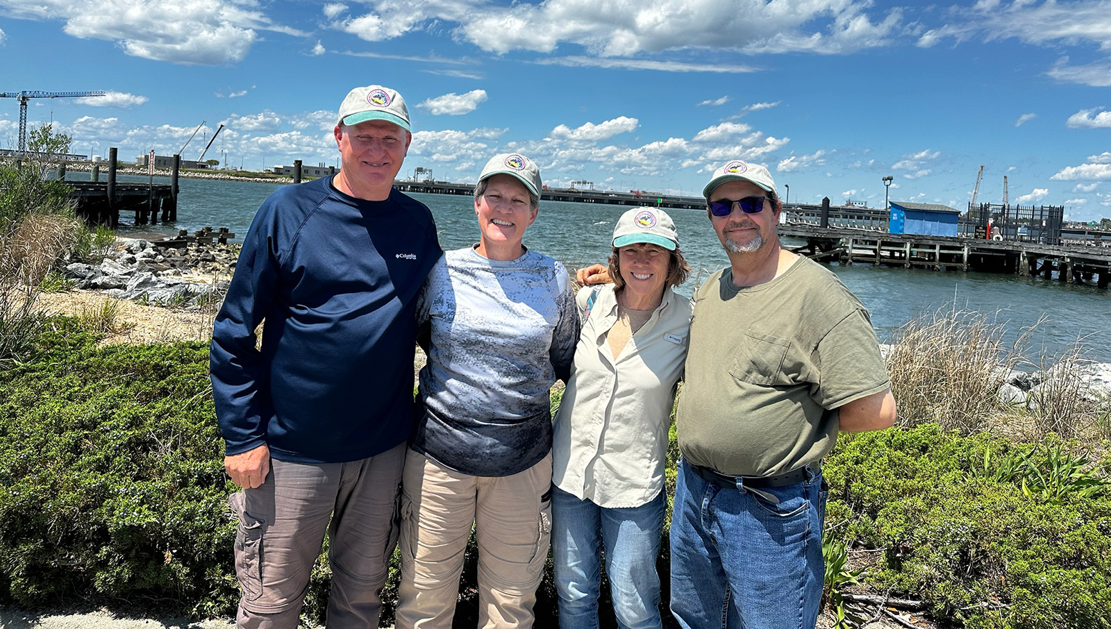 Una foto de cuatro personas sonrientes de pie en la playa de una isla con agua de fondo.