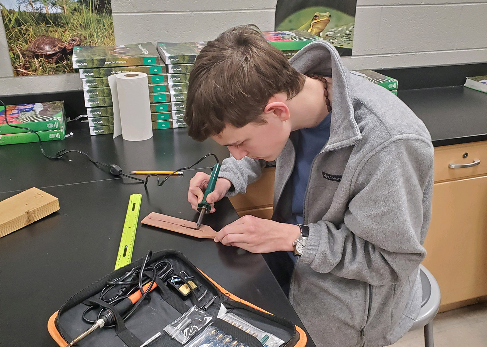 Una foto de un joven en una mesa de trabajo, usando una herramienta para quemar leña en una paleta de llamada de pavo.