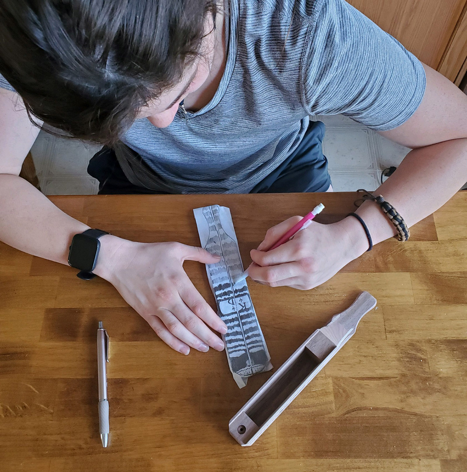 Una foto de una niña trazando un patrón en papel con una llamada de pavo de paleta sentada a su lado en la mesa.