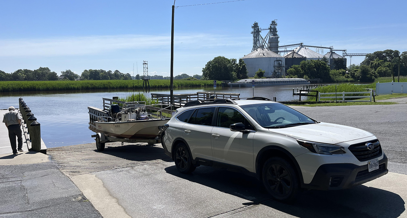 Una foto de un coche tirando de una pequeña lancha a motor y a punto de retroceder por una rampa para botes inclinada hacia el río.