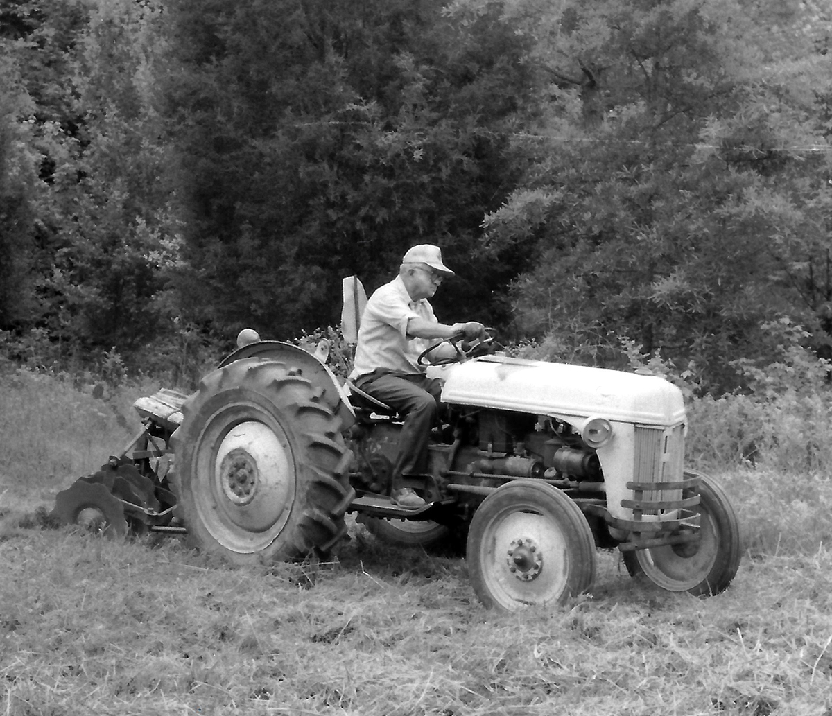 Una imagen en blanco y negro de un hombre con un tractor labrando un campo