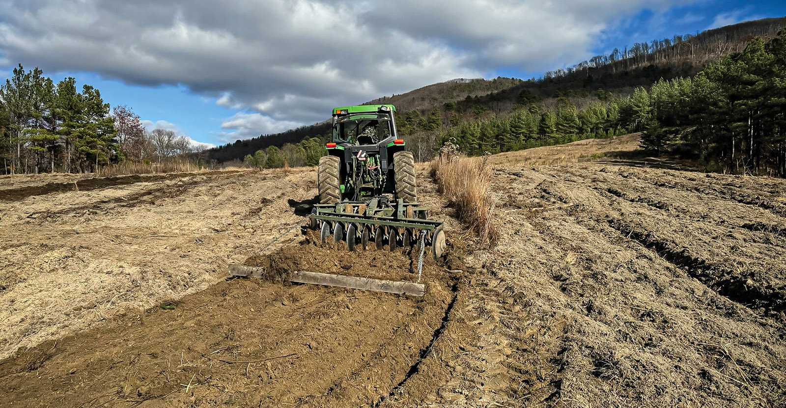 Una foto de un tractor tirando de una grada de discos a través de tierra abierta en un campo.