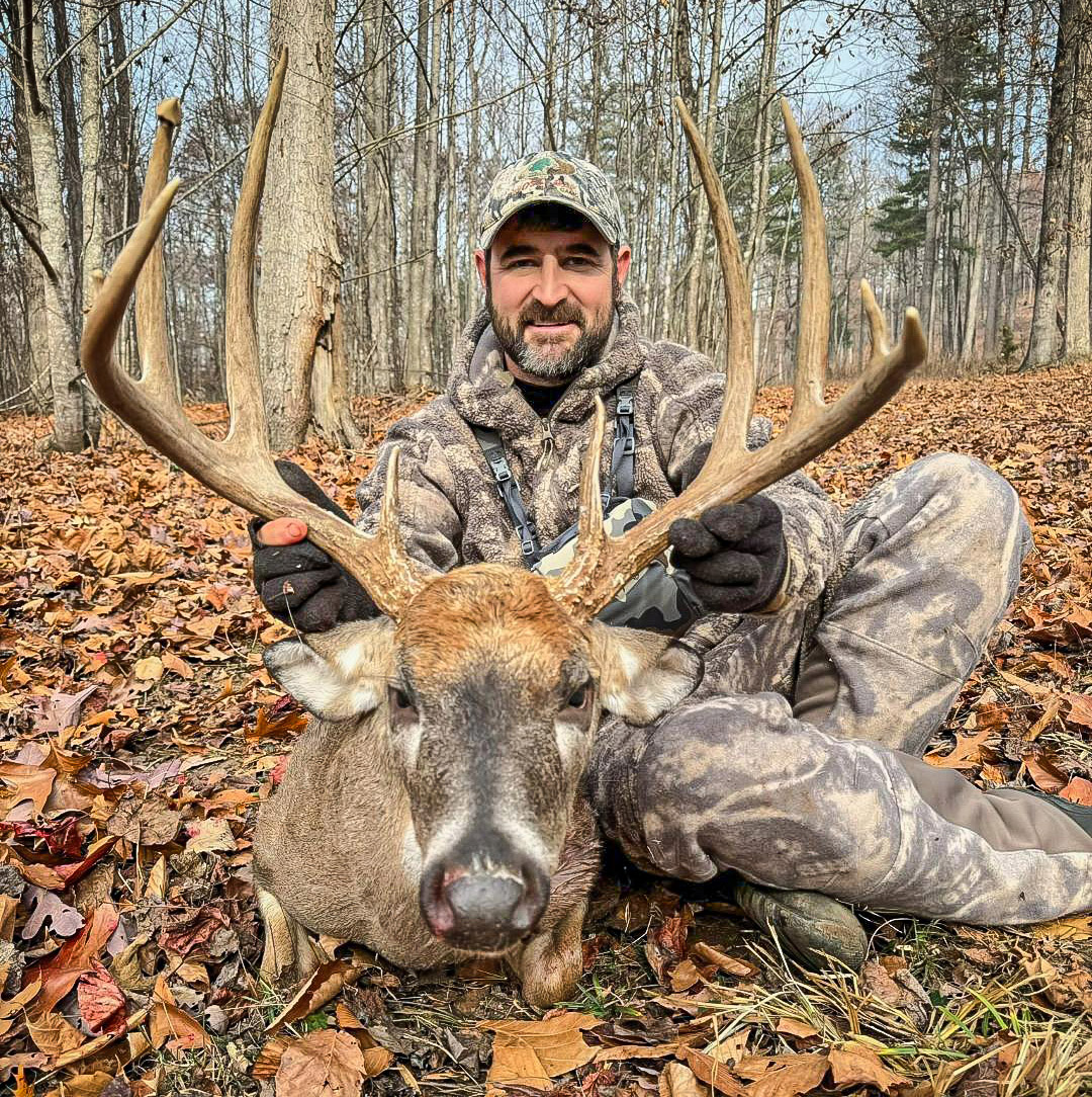 Una foto de un hombre camuflado y un gran ciervo de cola blanca.