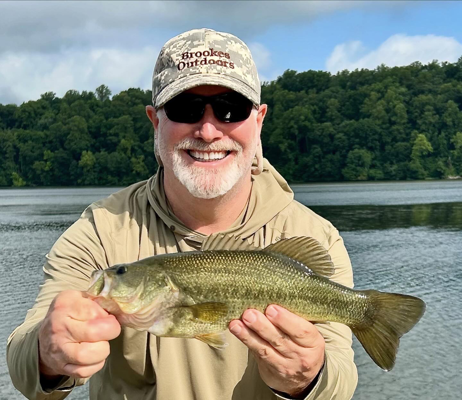 Un hombre sosteniendo una lubina frente a un río.