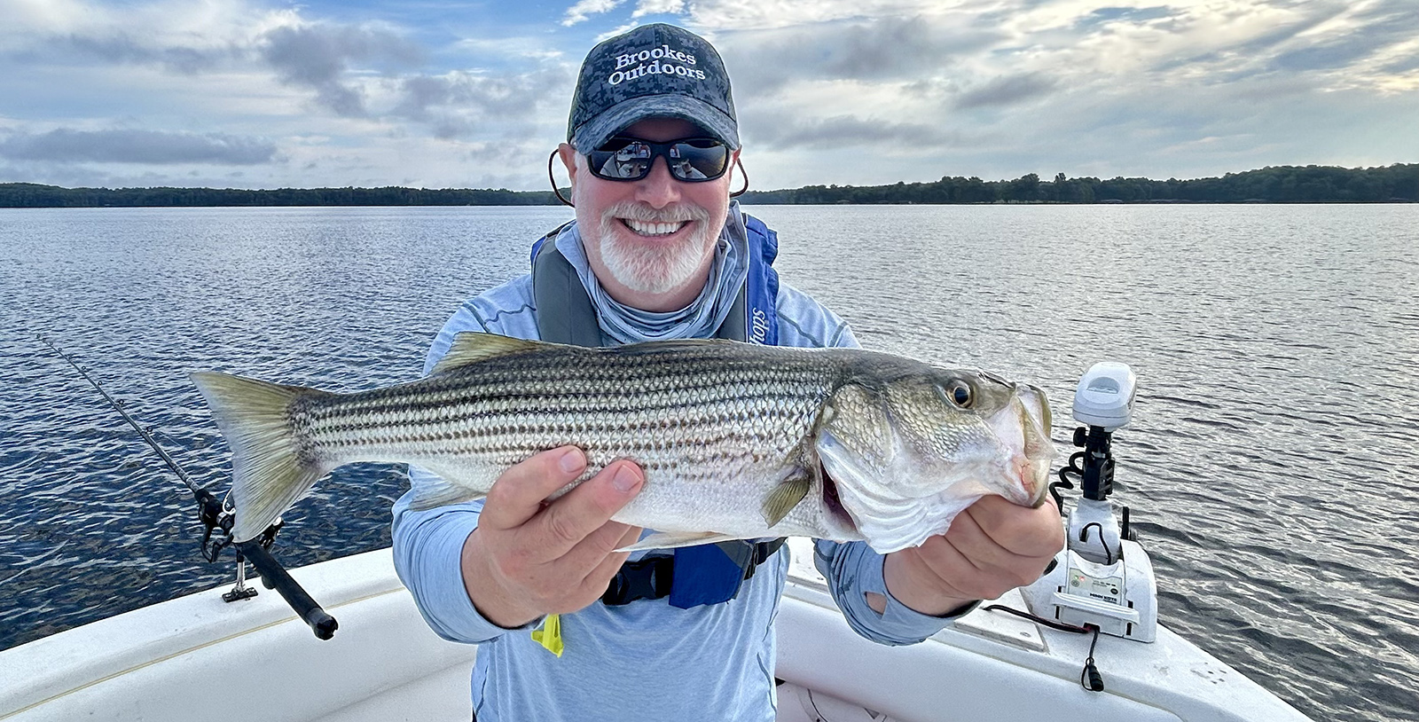 Un hombre sentado en un barco, sosteniendo una gran lubina rayada y sonriendo.