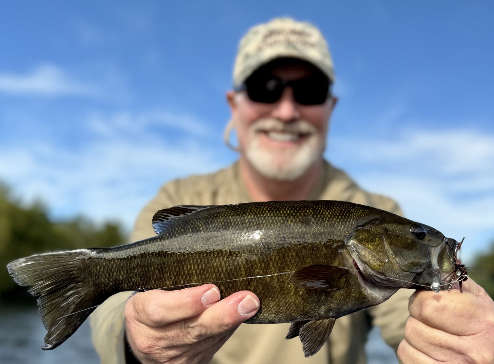 Una foto de un hombre sosteniendo una gran lubina de boca chica y sonriendo.