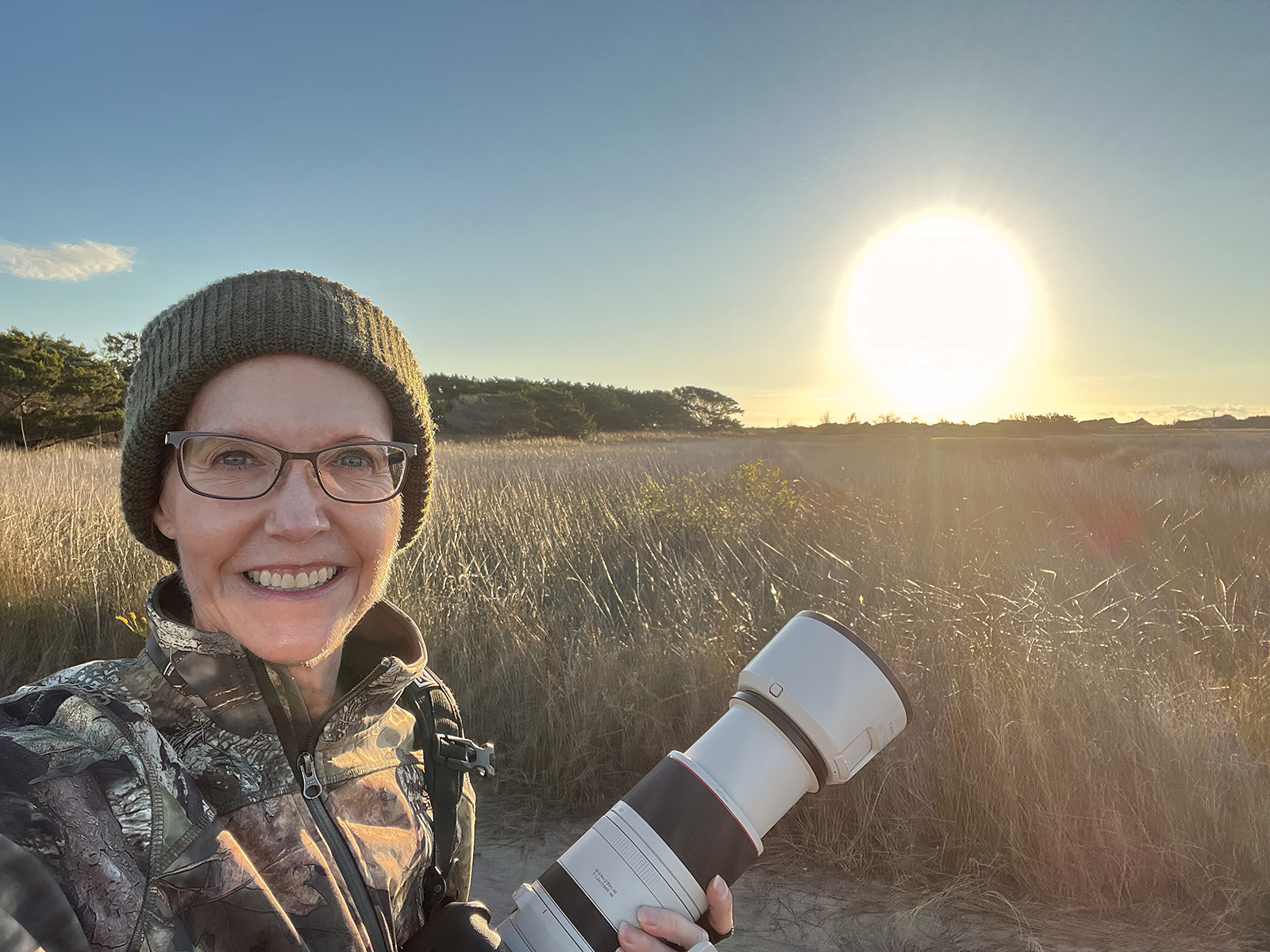 Una foto de una mujer sosteniendo una cámara al amanecer junto a un pantano.