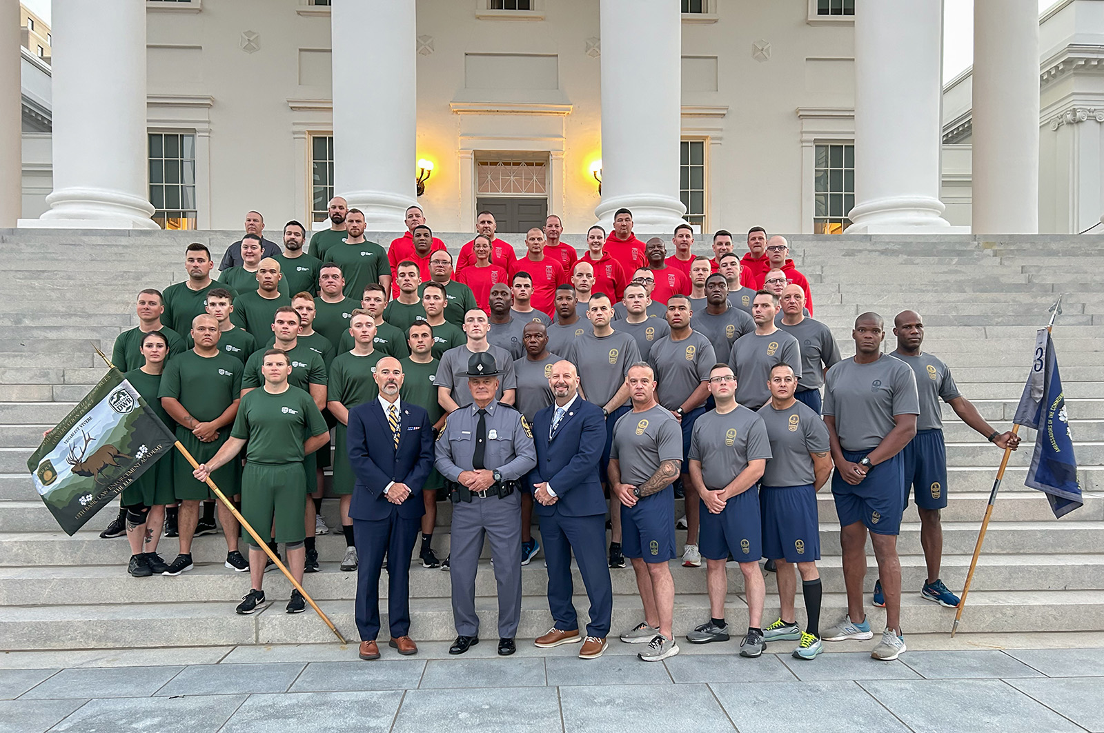 Una foto grupal de hombres y mujeres jóvenes en uniforme en los escalones del edificio del Capitolio de Virginia con tres hombres en traje y uniforme en la primera fila.
