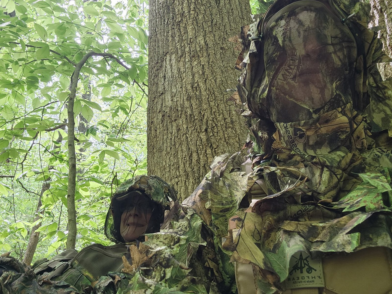 Una foto de dos mujeres en el bosque vistiendo camuflaje y pantallas faciales.