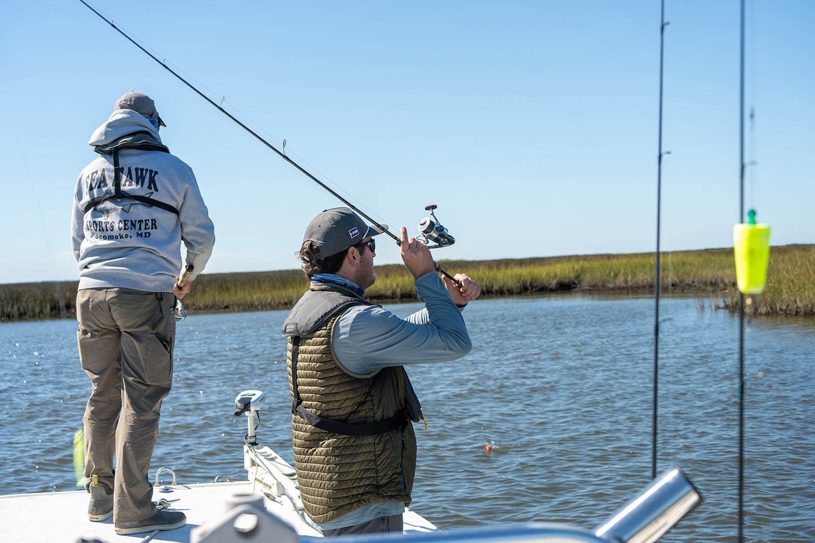 Una foto de dos hombres parados en la proa de un bote, pescando, con un pantano al fondo.