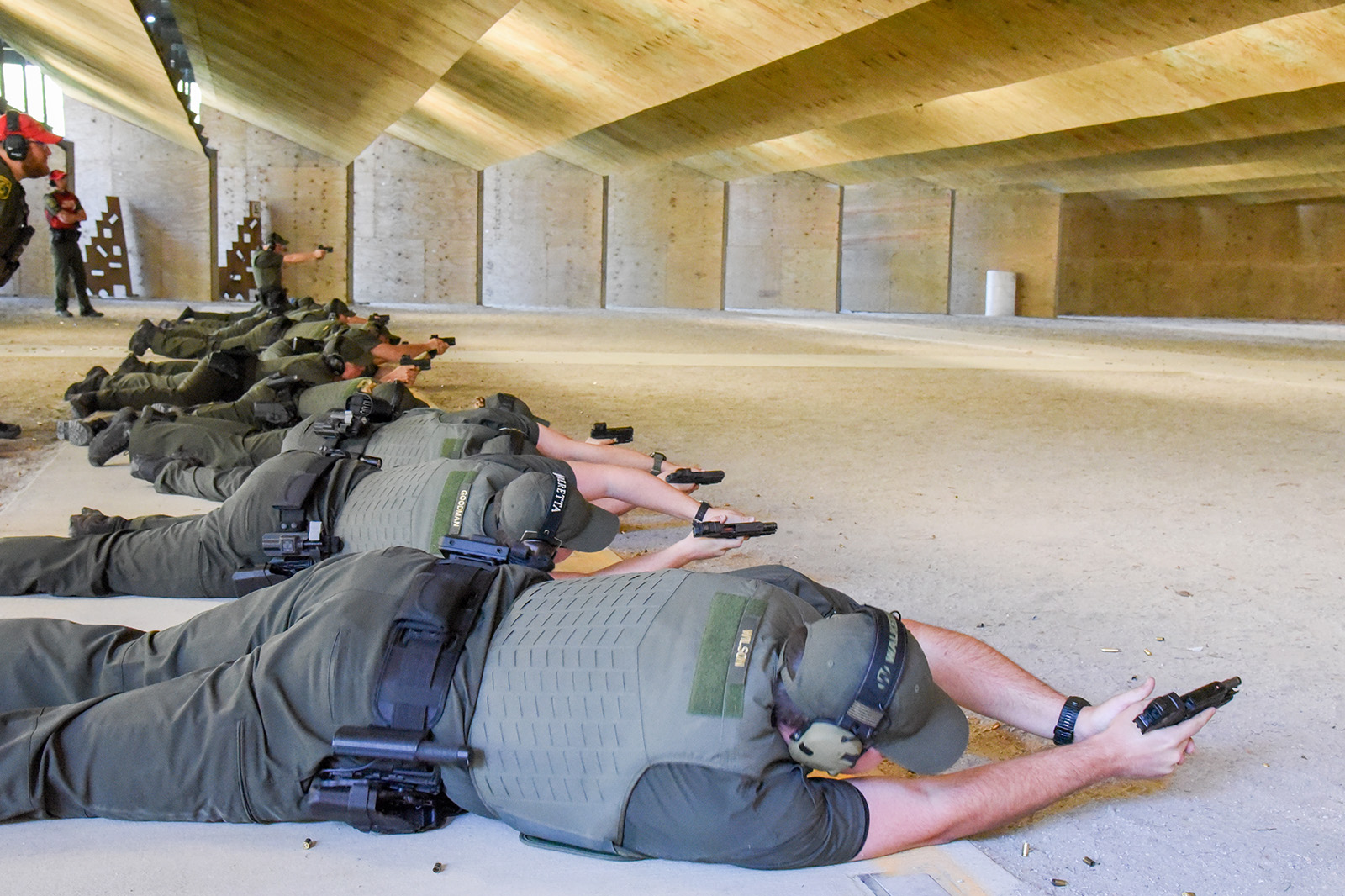 Una foto de una fila de hombres y mujeres en un campo de tiro, acostados de lado y apuntando con pistolas a los objetivos.