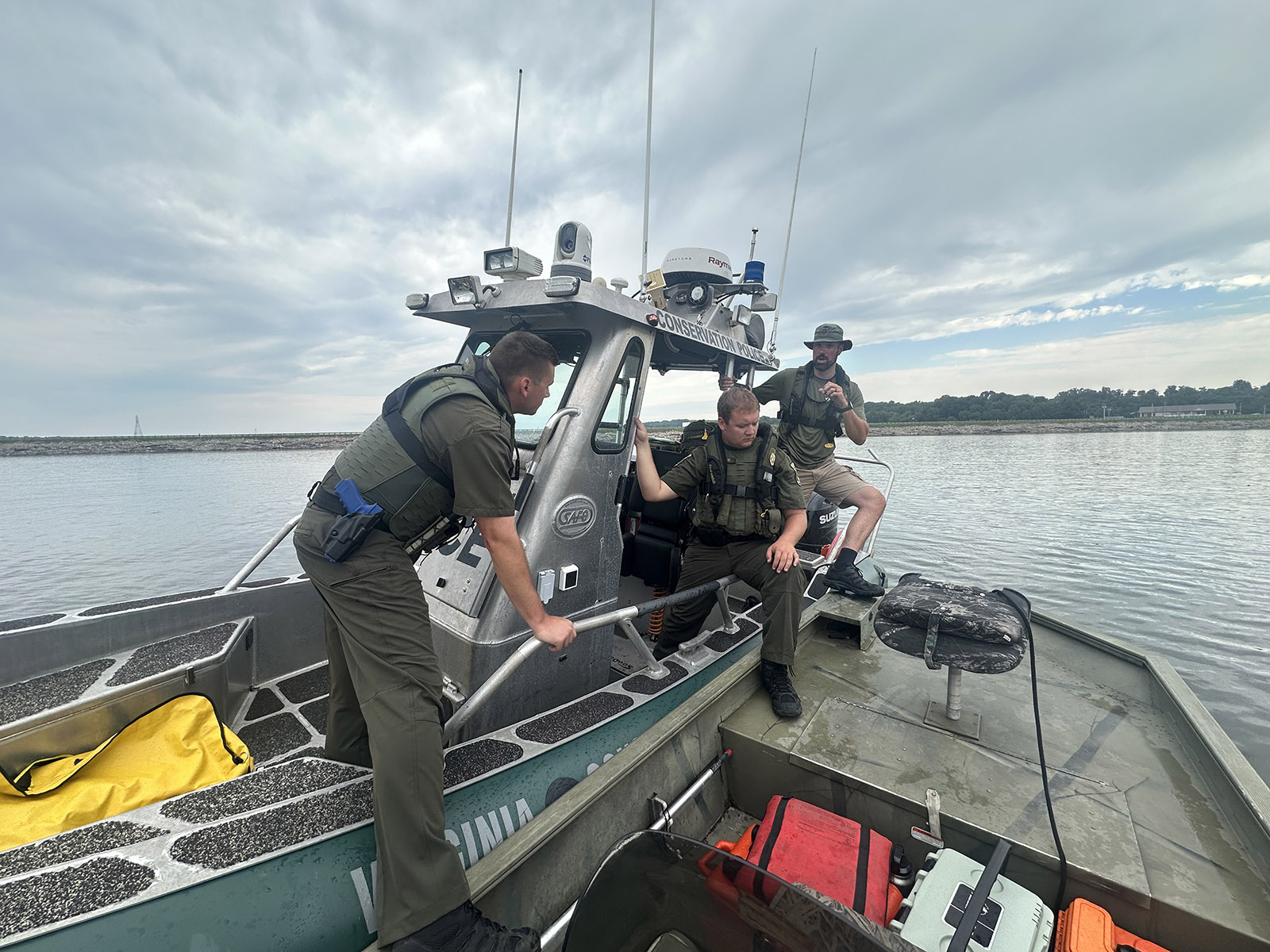 Una foto de tres hombres uniformados y chalecos salvavidas bajando de un barco de la Policía de Conservación a un barco más pequeño.